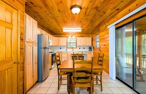 L’intérieur d’un chalet en bois comprend une cuisine, un coin repas et des portes-fenêtres coulissantes qui donnent sur une terrasse extérieure.