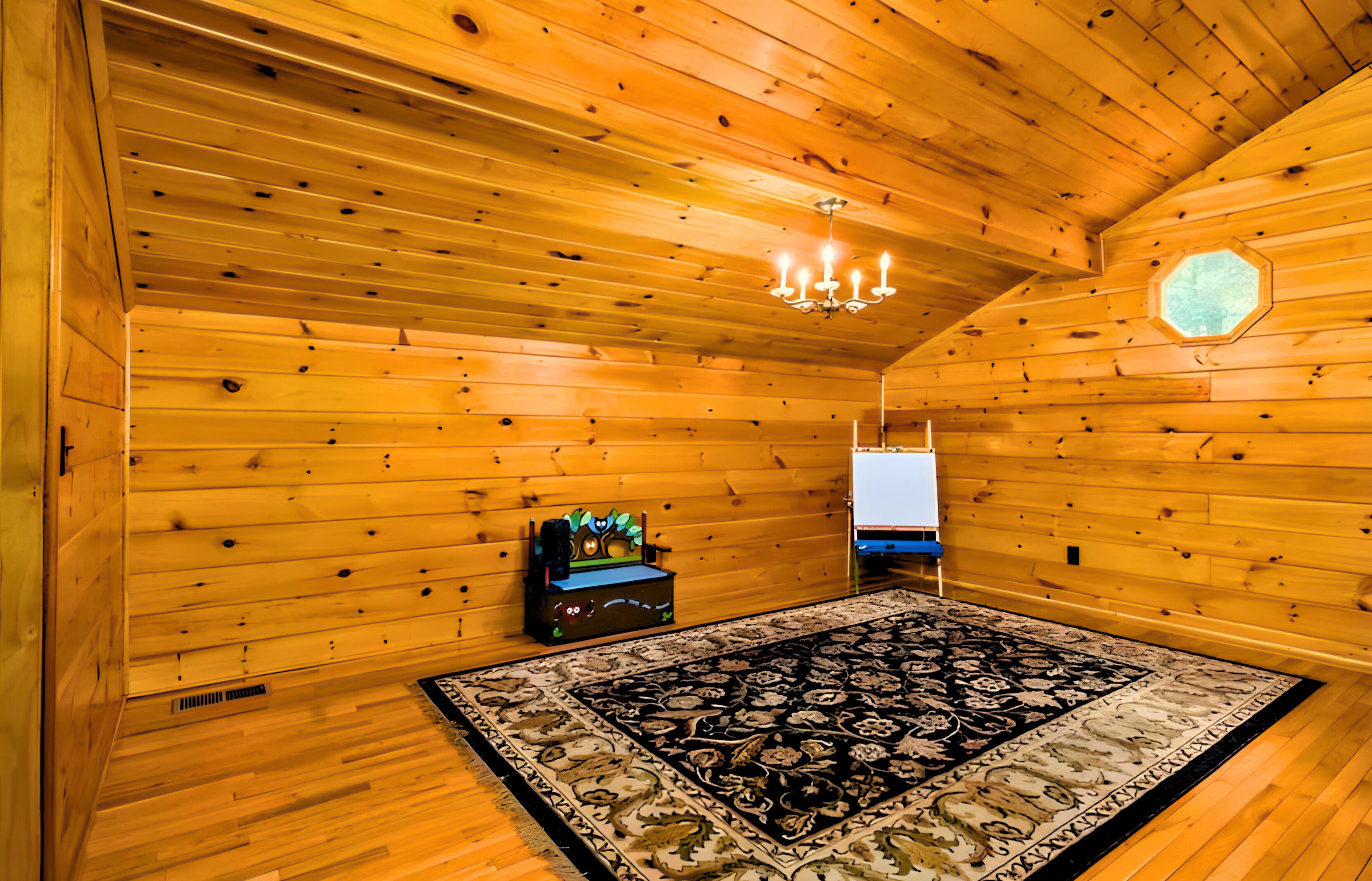 A log cabin room with wooden walls, a chandelier, a patterned rug, and a small table with a decorative item.