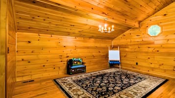 A log cabin room with wooden walls, a chandelier, a patterned rug, and a small table with a decorative item.