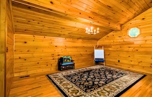Une chambre de style rustique, avec des murs en bois, un lustre, un tapis à motifs et une petite table agrémentée d’un objet décoratif.