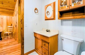 Une salle de bain aux murs lambrissés, équipée de toilettes, d’un lavabo et d’un meuble de rangement.