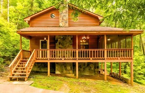 Une cabane en bois avec une cheminée en pierre, un balcon et un escalier menant à l’entrée.