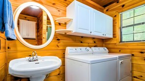 Een houten badkamer in een vakantiehuisje, met een wastafel, spiegel, kast en wasmachine.