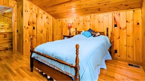 Een slaapkamer met houten lambrisering, een bed, een nachtkastje en een lamp.