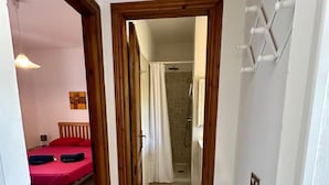 A narrow hallway leading to a bathroom with a shower and a bed with red bedding. - Villetta Oasi La Cinta Centro (San Teodoro)