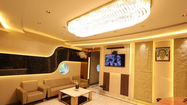 A modern lobby with a sofa, a coffee table, a TV, and a chandelier. - Hotel Moti (Mau Ranipur)