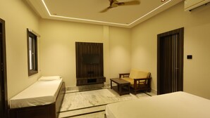 A bedroom with a bed, a chair, a small table, a ceiling fan, and a TV. - Hotel Moti (Mau Ranipur)
