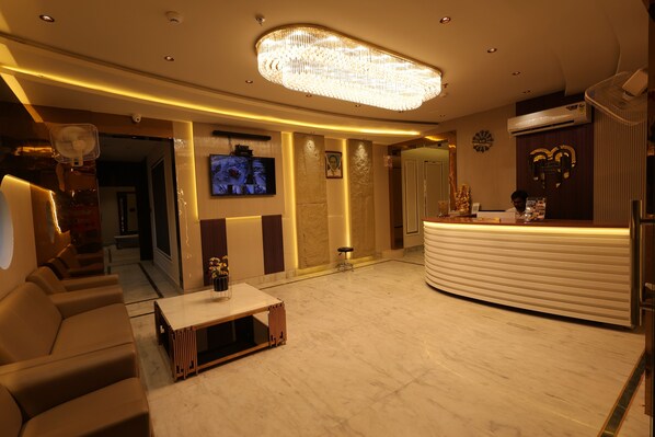 A hotel lobby with a reception desk, seating area, and a television screen. - Hotel Moti (Mau Ranipur)