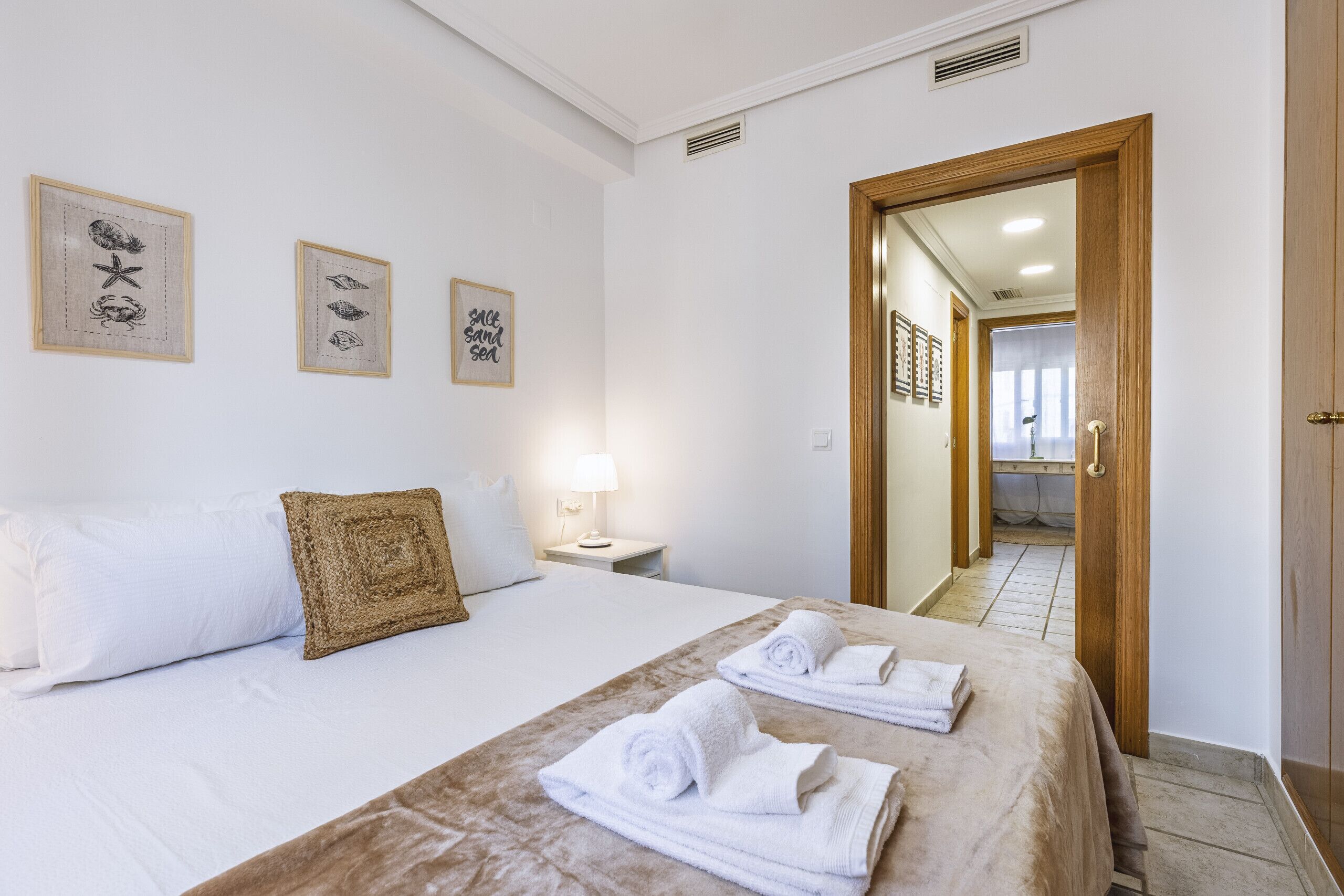 Une chambre d’hôtel avec un lit, deux serviettes, une table de chevet, une lampe et des tableaux encadrés au mur.