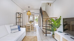 Una sala de estar moderna con un sofá blanco, una mesa de comedor y una escalera que sube a otro nivel.