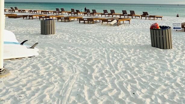 Une plage avec des rangées de chaises longues en bois et une poubelle.