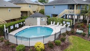 Zona residencial con piscina rodeada por una valla, casas al fondo y un letrero que indica ausencia de socorrista.