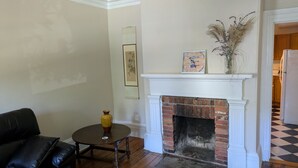 A living room with a fireplace, a black leather sofa, a small round table, and a vase with dried plants. - Townhouse 3 at Historic Bauer Terrace (Halifax)