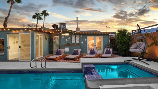 A pool area with lounge chairs and a small pool, surrounded by a house with string lights and palm trees. - Eclectic Bohemian Maximalist Pad with Pool and Spa (Desert Hot Springs)