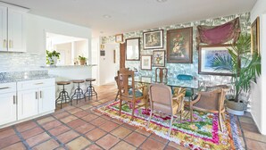 A kitchen with white cabinets, a tiled backsplash, and a dining area with a colorful rug and wooden chairs. - Eclectic Bohemian Maximalist Pad with Pool and Spa (Desert Hot Springs)