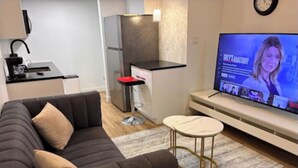 A modern living room with a dark sofa, a small round table, and a television displaying a program. - Home away from Home (Edmonton)