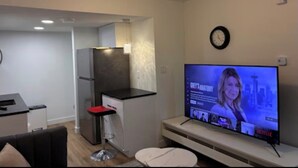 A modern living room with a flat-screen TV, a dining area, and a kitchen. - Home away from Home (Edmonton)