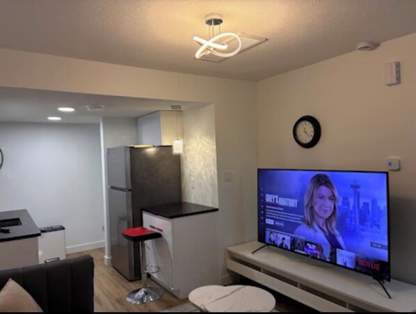 A modern living room with a flat-screen TV, a dining area, and a kitchen.