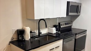 A compact kitchen with a black countertop, white cabinets, a microwave, a toaster, and a dishwasher. - Home away from Home (Edmonton)