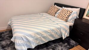 A bed with a striped bedspread, two polka-dotted pillows, a dark wooden nightstand, and a black furry rug. - Home away from Home (Edmonton)