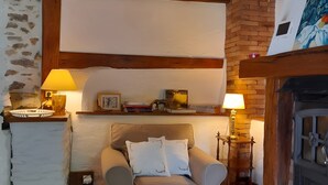 A cozy room with a sofa, a small table with a lamp, a fireplace, and a stone wall.