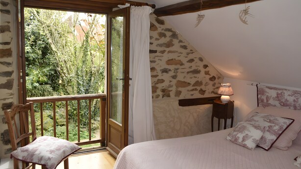 A bedroom with a stone wall, a wooden chair, a bed with floral bedding, and a view of greenery through a glass door.