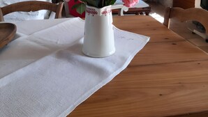 A wooden table with a white placemat, a white vase with a floral arrangement, and a rustic interior with exposed beams and a window.