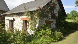 A stone house with a sloped roof, wooden shutters, and a garden in front.