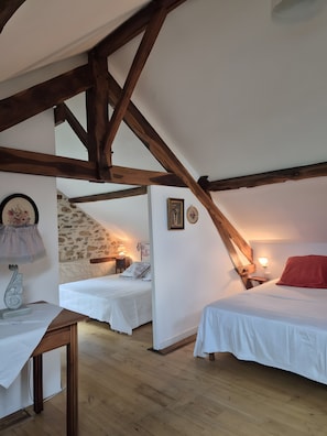 Quarto com duas camas, vigas de madeira, parede de pedra e uma pequena mesa com abajur.