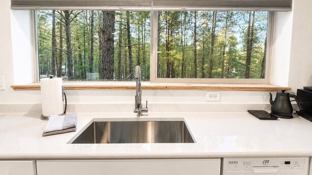 Une cuisine équipée d’un évier en acier inoxydable, d’une fenêtre donnant sur les arbres, d’une bouilloire et d’un égouttoir à vaisselle.