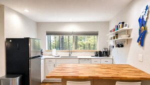 Une cuisine moderne dotée d’un îlot central en bois, d’appareils électroménagers en acier inoxydable et offrant une vue sur la forêt.