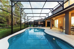 Ein Schwimmbad mit Glasveranda, umgeben von einer Terrasse mit Gartenmöbeln.
