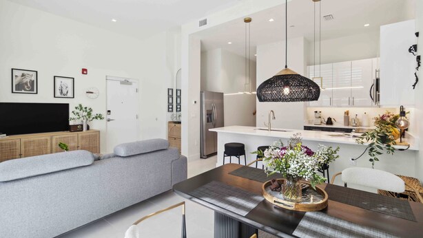 Una sala de estar moderna con un sofá gris, una mesa de comedor con un florero y una zona de cocina al fondo.
