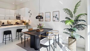 Una cocina moderna con armarios blancos, un comedor con mesa negra y una planta grande en maceta.