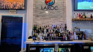 Zona de bar con una variedad de botellas de licor, una pantalla de televisión y un letrero que dice 'THIS IS OUR HAPPY PLACE'.