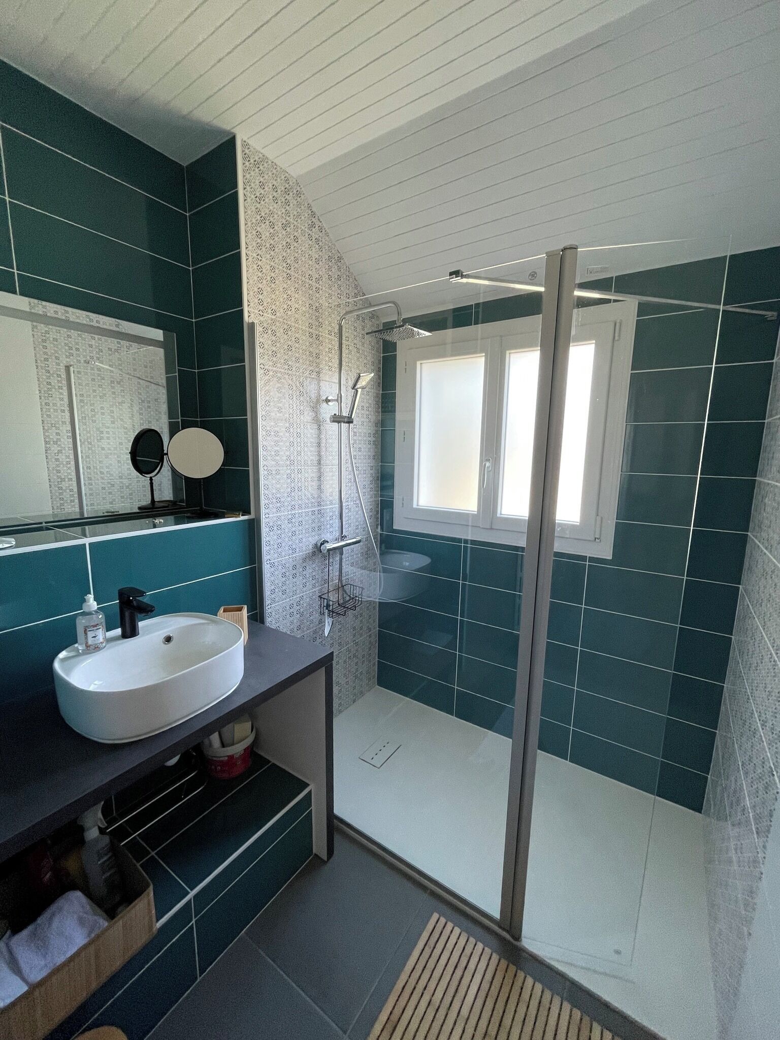 Une salle de bain moderne avec une douche à parois de verre, un lavabo avec un miroir et des carreaux de couleur turquoise.