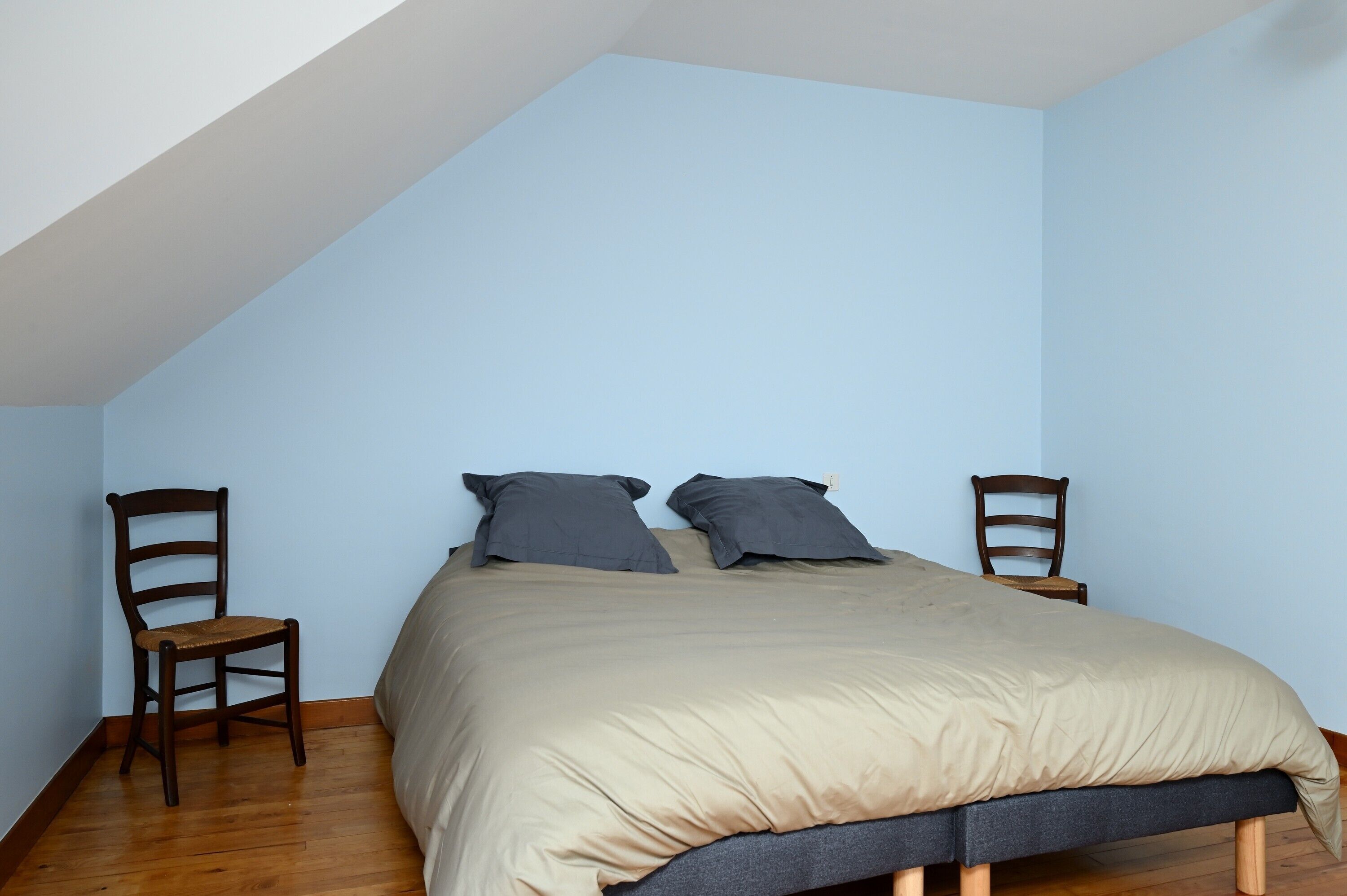 A bedroom with a bed, two chairs, and a sloped ceiling.