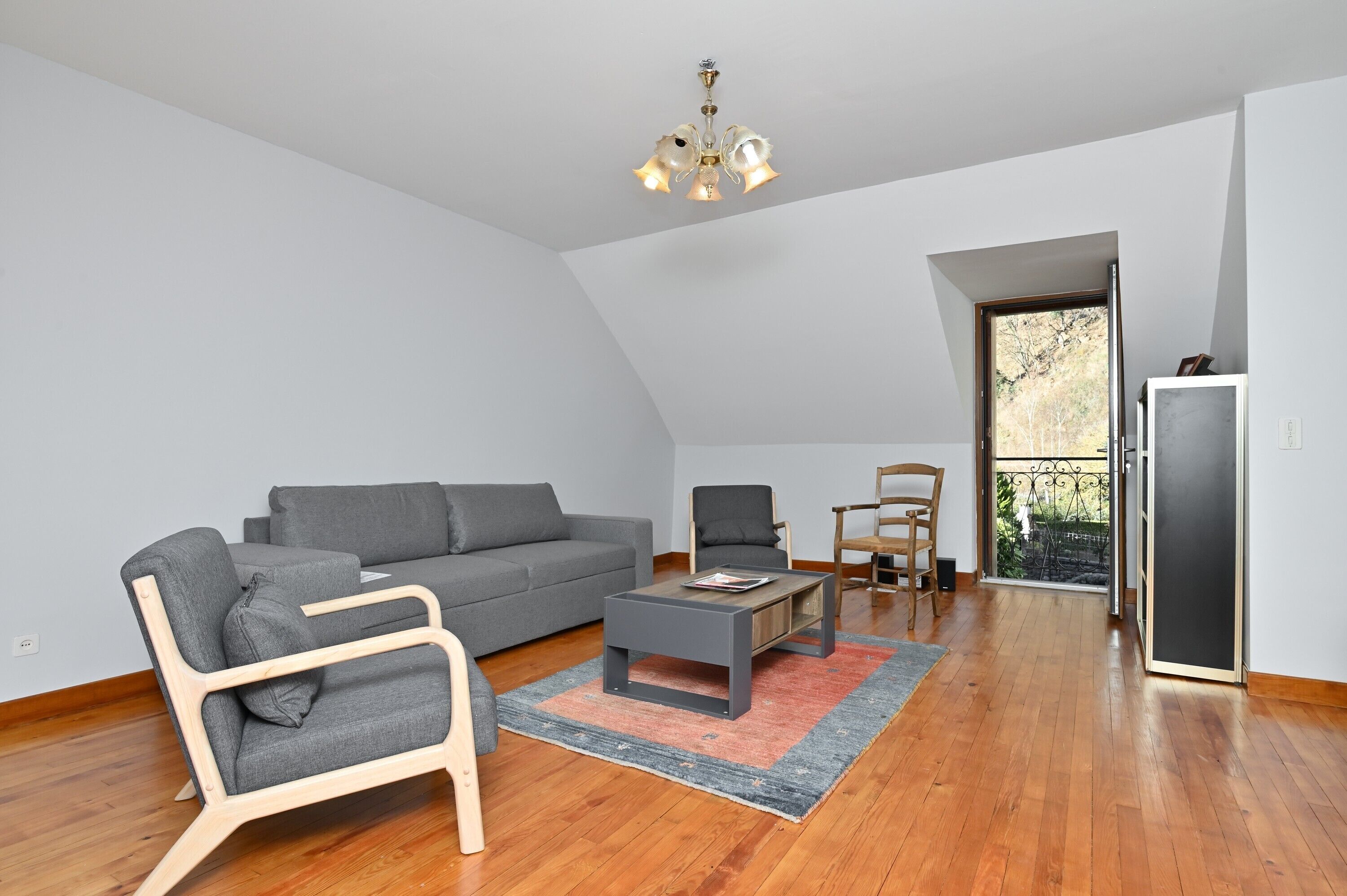 Un salon moderne avec un canapé gris, une chaise en bois, une table basse et un lustre.