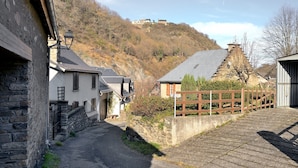 A narrow street with stone buildings, a wooden fence, and a hill with a building in the background. - Holiday Home "Gîte à Cazaux - Bagnères de Luchon" with Private Garden (Cazaux-Layrisse)