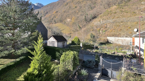 A mountainous landscape with a small building, a fenced area, and a road. - Holiday Home "Gîte à Cazaux - Bagnères de Luchon" with Private Garden (Cazaux-Layrisse)