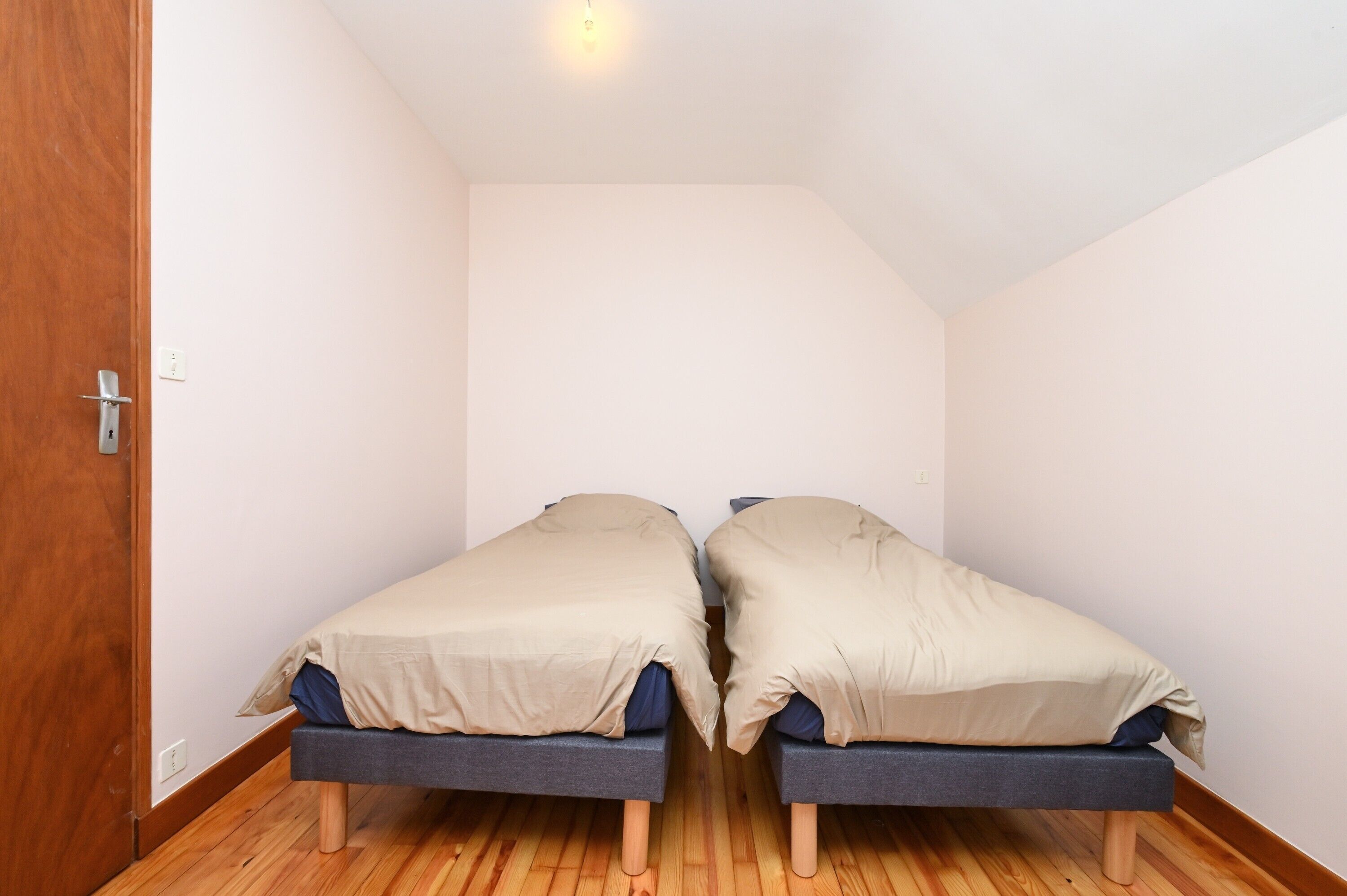 Une chambre avec deux lits simples, un plancher en bois et une porte en bois.