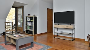A modern living room with a large flat-screen TV, a bookshelf, a wooden chair, and a coffee table. - Holiday Home "Gîte à Cazaux - Bagnères de Luchon" with Private Garden (Cazaux-Layrisse)