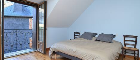 Une chambre avec un lit, deux chaises, un balcon doté d’une rambarde en métal et un plancher en bois.