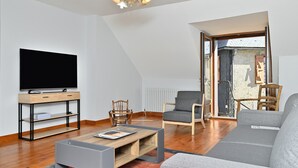 A modern living room with a flat-screen TV, wooden furniture, and a large window. - Holiday Home "Gîte à Cazaux - Bagnères de Luchon" with Private Garden (Cazaux-Layrisse)