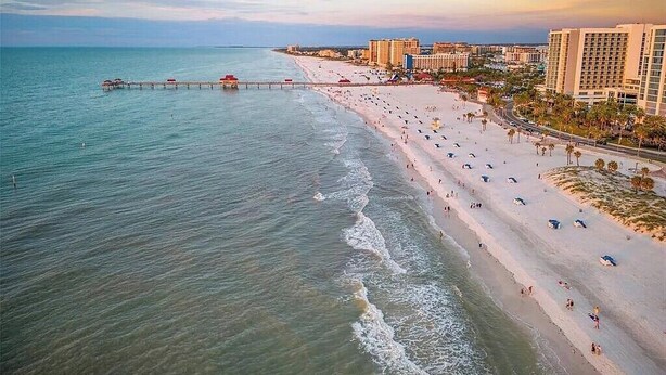 A beach with a pier extending into the water, adjacent to a row of hotels.