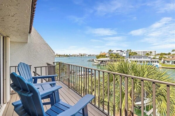 A balcony with blue Adirondack chairs overlooking a marina with boats and a dock.