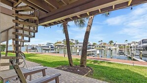 A covered outdoor area with a wooden bench, a spiral staircase, and a view of a marina with boats and palm trees.