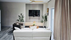 Una sala de estar moderna con un sofá, una mesa de centro, un televisor montado en la pared y un ventilador de techo.