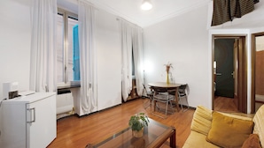 Ein Wohnzimmer mit einer Couch, einem Couchtisch, einem Esstisch mit Stühlen und einer Küchenzeile mit Kühlschrank.