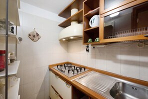 A kitchen with a gas stove, stainless steel sink, wooden cabinets, and a tiled backsplash.